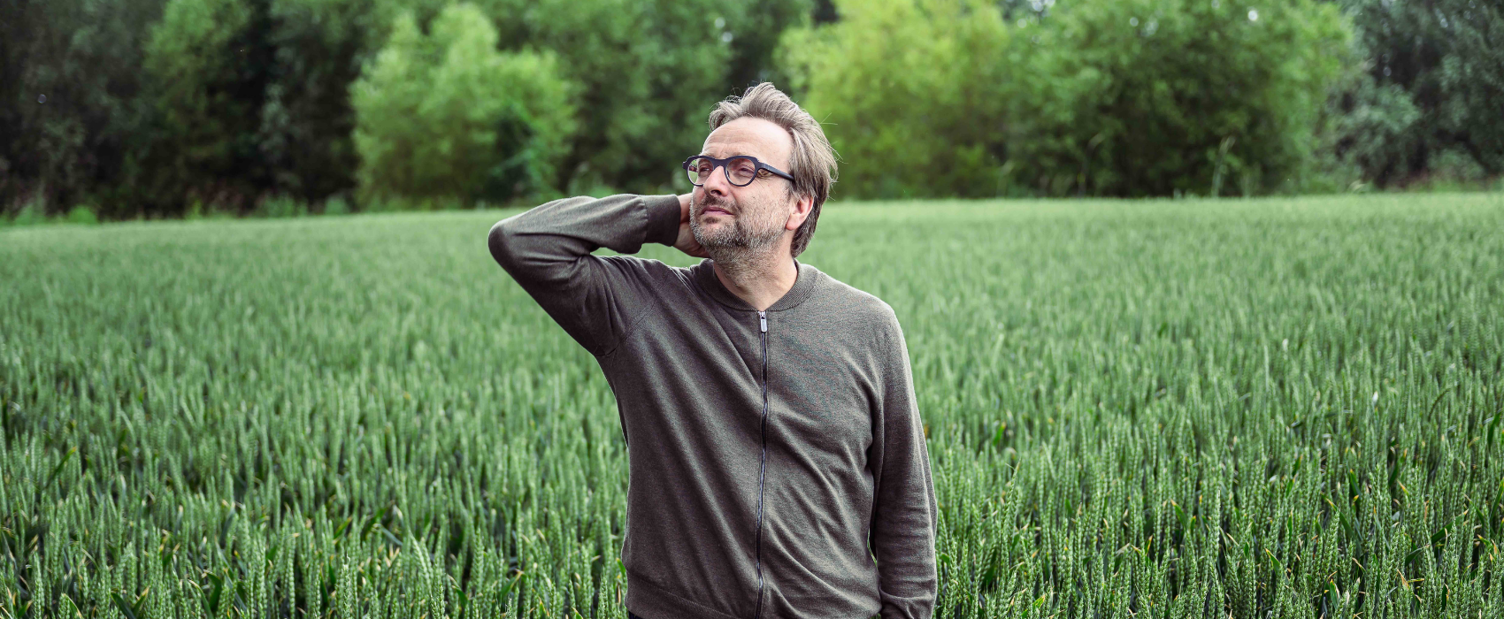 Auteur Bart Van Loo, foto in een veld met bomen op de achtergrond